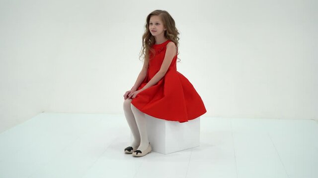 Charming Blonde Girl in Dress Sitting on White Cube