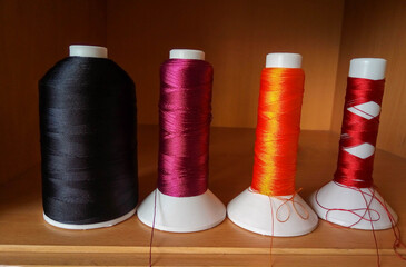 Multicolored sewing threads in bobbins stand on a brown shelf.