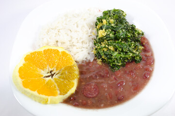 Feijoada brasileira servida com laranja, couve e arroz em um prato branco