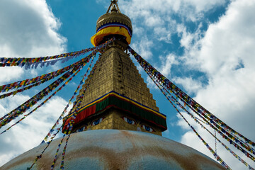 The upper part of the Boudhanath stupa in Kathmandu, Nepal. The image of Buddhas eyes on a gold surface of the stupa. Colorful prayer flags nearby.