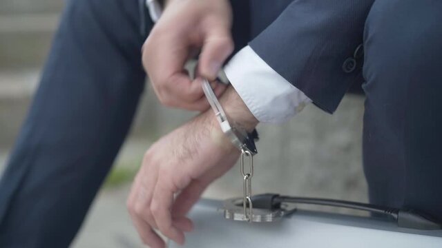 Close-up of male hand chained to attache case with handcuffs. Unrecognizable secret agent with governmental secrecy materials, or symbol of overworked businessman inseparable from work.