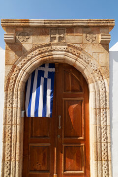 A Greek flag hangs under the stone archway in the doorway of one of the captain's houses of Lindos on Rhodes, Dodecanese, Greek Islands, Greece