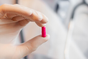 Doctor hand in sterile gloves holding pill on white background close up view