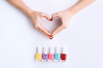 Nail Polish. Art Manicure. Multi-colored Nail Polish Bottles in row with female hands in heart shape. Top view