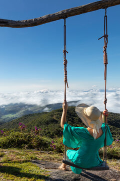 A young woman using a swing over a view of rainforest-covered mountains in the Ibitipoca Reserve, Minas Gerais, Brazil