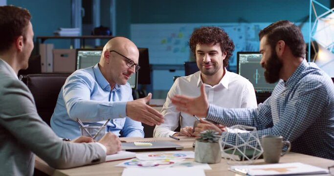 Group of businessmen sitting at table and negotiating. Business meeting ends with handshake between two adult men.