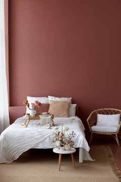 Bedroom interior of wicker armchair, bed and small wicker table on it for breakfast with a pink wall in the background