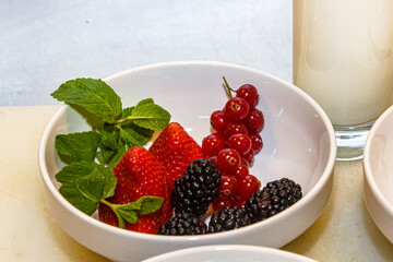 Strawberries, blackberries and red currants with mint are in a white bowl