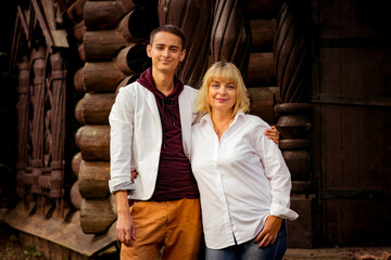 Fototapeta na wymiar A beautiful woman,blonde,middle-aged,in a white shirt and jeans,with a large son,stands near an eco-friendly wooden house