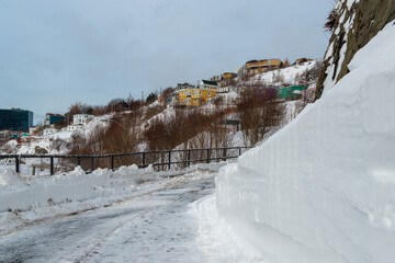 A narrow street in St. John's, Newfoundland with colorful wooden homes buried in fresh white snow from a storm on a hill. The street has been plowed but the snow is piled up alongside a cliff. 