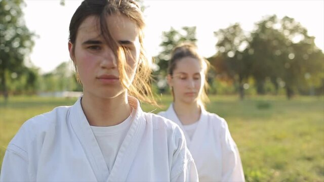 A young girl looks at the camera while meditating in a karate class while the other continues to sit with her eyes closed. Close-up. Slow motion. The camera changes focus