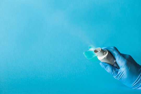 Blue asthma inhaler with aerosol spray of particles flicker in hand, on a blue background. A pharmaceutical product for treating preventing an asthma attack. Minimal style. Space for copy.