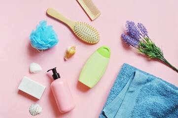 Many bath products on a pink background. Flat lay composition beauty photo soap, green shampoo bottle, hair balm, blue sponge, wooden hair brushes, lavender flowers and cotton towel