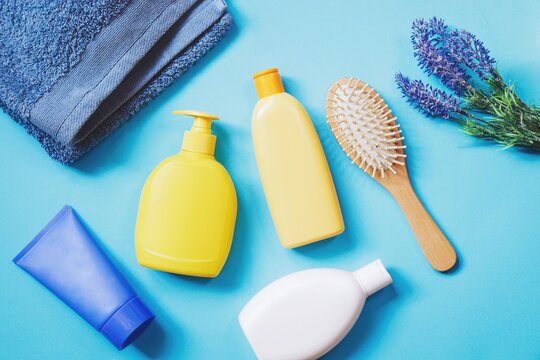 Flat lay composition photography cosmetics for hair and skin care. Natural bath products. Shampoo, liquid soap, moisturizing cream, wooden hairbrush, and lavender flowers on a blue background