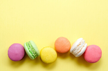 Sweet and colorful multicolored French macarons on a yellow background lined in a line, dessert with tea or coffee. place for text. view from above