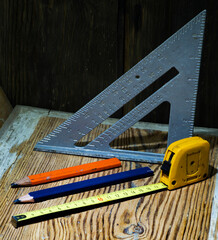 triangle, measuring tape and contractors pencils on a wooden background