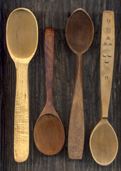 Four empty wooden spoons of different sizes on dark background. Close up.