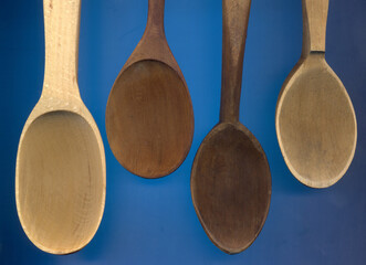 Four empty wooden spoons of different sizes on blue background. Close up.