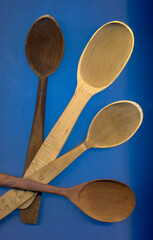 Four empty wooden spoons of different sizes on blue background. Close up.