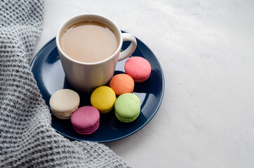 Obraz na płótnie Canvas Background with gray plaid, coffee with milk, cappuccino and multi-colored appetizing macaroons, top view, copy space. home comfort, warmth, care, tenderness.