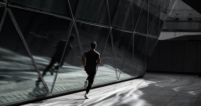 Male runner runs in city beside a glass architecture