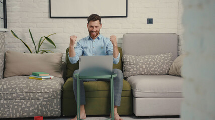 Happy man reading good news on laptop computer sitting on sofa at home businessman positive success communication table modern worker smiling slow motion