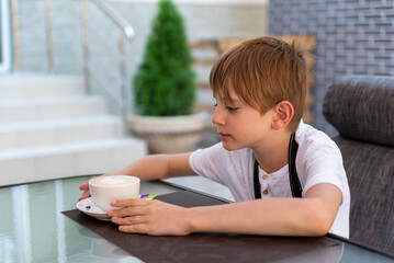 Fototapeta na wymiar Boy is drinking coffee in cafe. Child in restaurant. Independent teenager