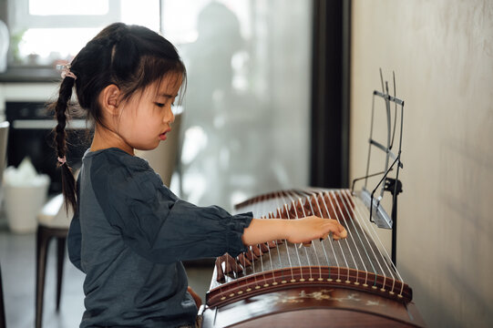 Cute little playing traditional musical instrument zither at home