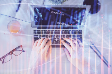 Double exposure of man's hands typing over laptop keyboard and forex chart hologram drawing. Top view. Financial markets concept.