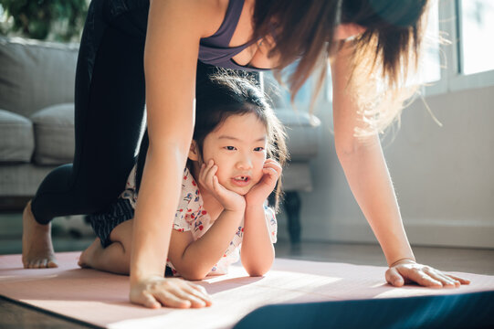 Asian young mom and daughter practicing yoga at home