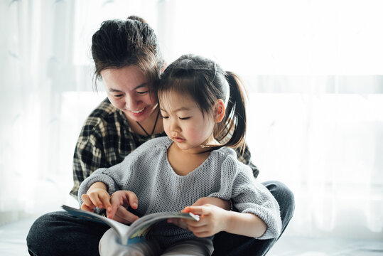 Young mother and her toddler girl reading at home
