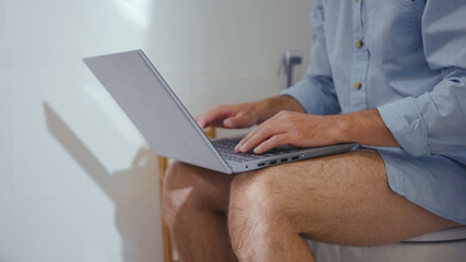 Sad businessman working on laptop wearing mask sit on the toilet at home restroom bearded serious wc isolation quarantine pandemic coronavirus covid-19 portrait close up slow motion