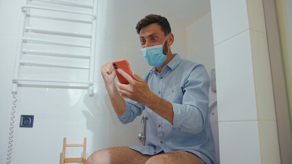 Happy businessman with mask use phone sitting on the toilet smiling mobile restroom smartphone...