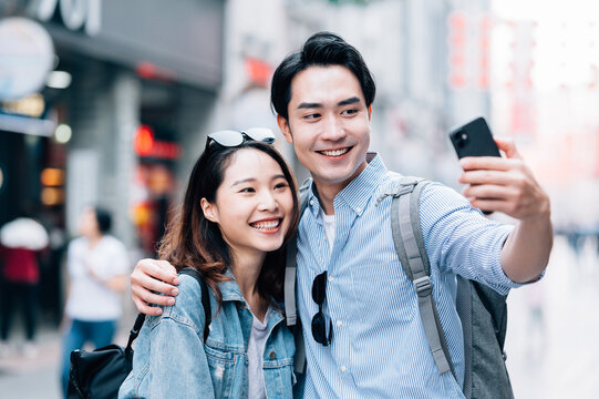 Young asian couple traveling in a city downtown and taking selfie with cell phone