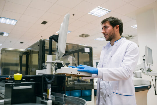 Side view of man in white coat using sample analyzer while working in modern lab.