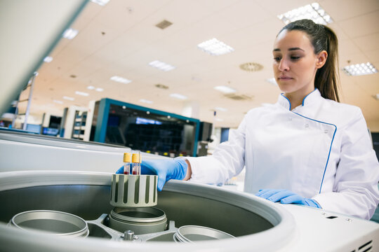 Beautiful young woman in lab robe and putting blood samples in analyzer while working in modern laboratory.