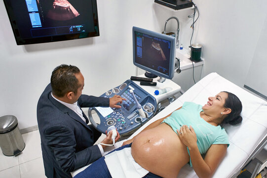 Happy pregnant mom sees her unborn child on an ultrasound screen on the wall