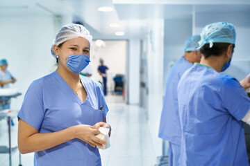 Doctor with mask smiling at the camera. Other doctors washing their hands in the background