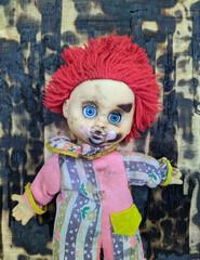 scary and old battered clown doll with burnt face and red hair on the background of burnt wooden board