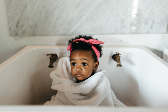A cute toddler sitting in a farmhouse sink, wrapped in a towel. Bath time.