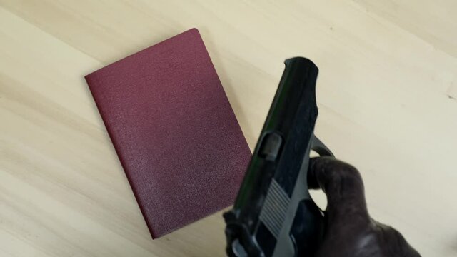 A hand in black glove putting nternational passport of the Russian Federation and gun Makarov pistol on a table as a symbol of Russian crime