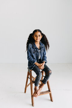 Studio portrait of a black girl sitting on a step stool with white background.