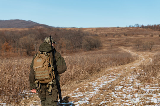Anonymous hunter walking on snowy path in field