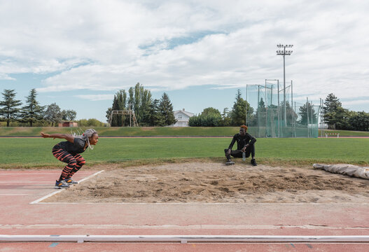 African American sportswoman preparing to jump into sandpit near instructor