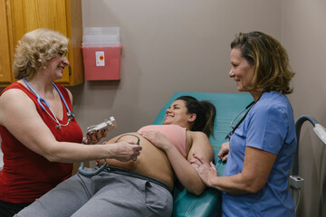Midwife Examining Pregnant Mother at Pregnancy Clinic with Doula at Her side