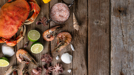 Top view of seafood banner with crab, shrimps, octopuses, lime, lemon, seashells and sea salts on rustic wooden background. Tasty meal concept. Flat lay.