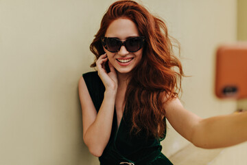 Fototapeta premium Ginger woman in sunglasses smiling and taking selfie