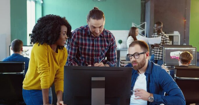 Three office workers: one girl and two men, laughing looking at computer screen. Young team brainstorming over design project.