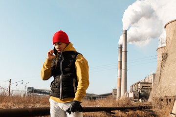 Ethnic man speaking on smartphone near factory