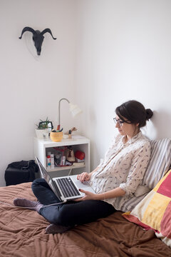 Portrait of a young female model laying on the bed and using laptop